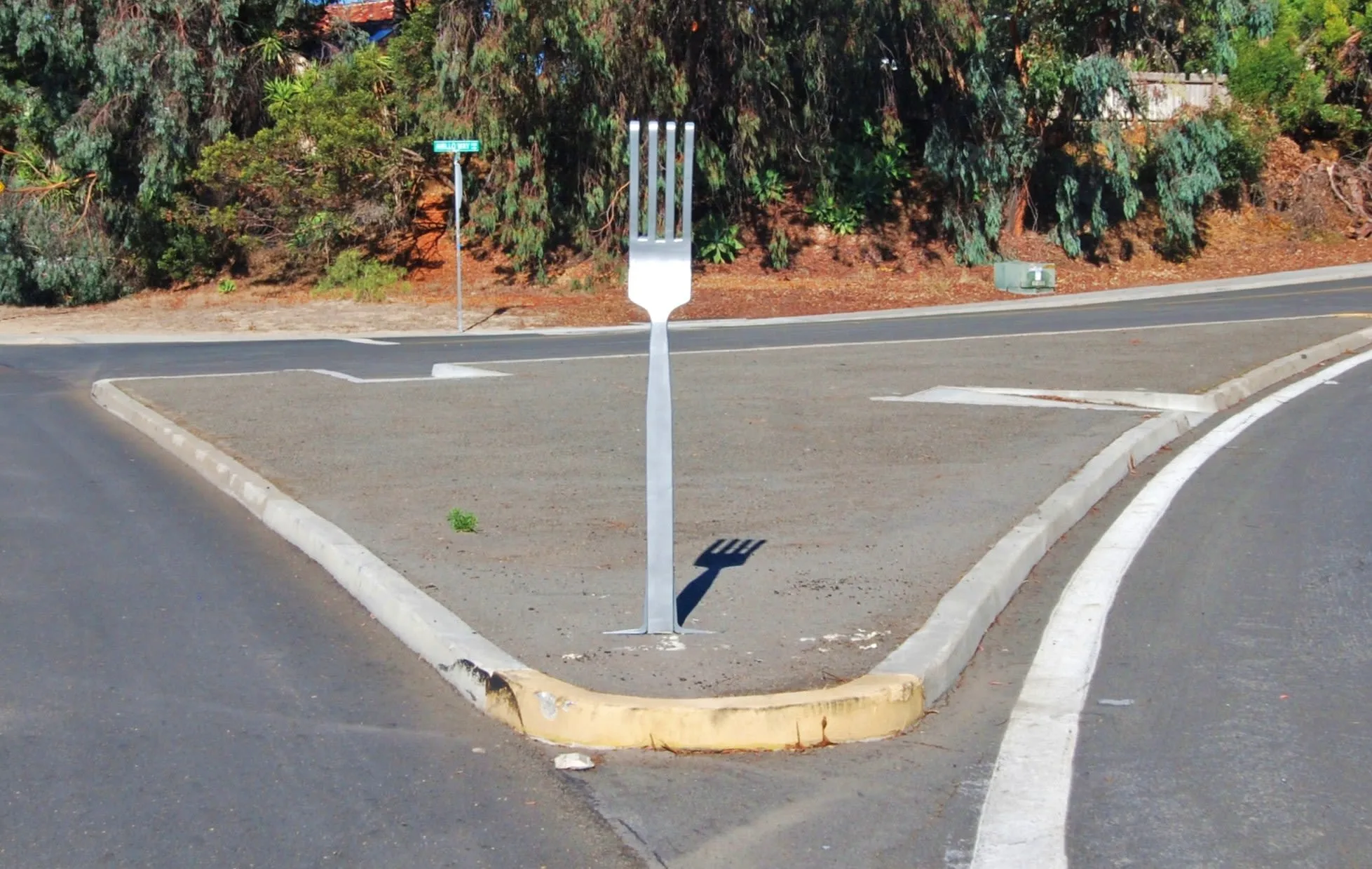 An oversized metal fork standing upright in the pavement of a traffic island, where one road forks into two.