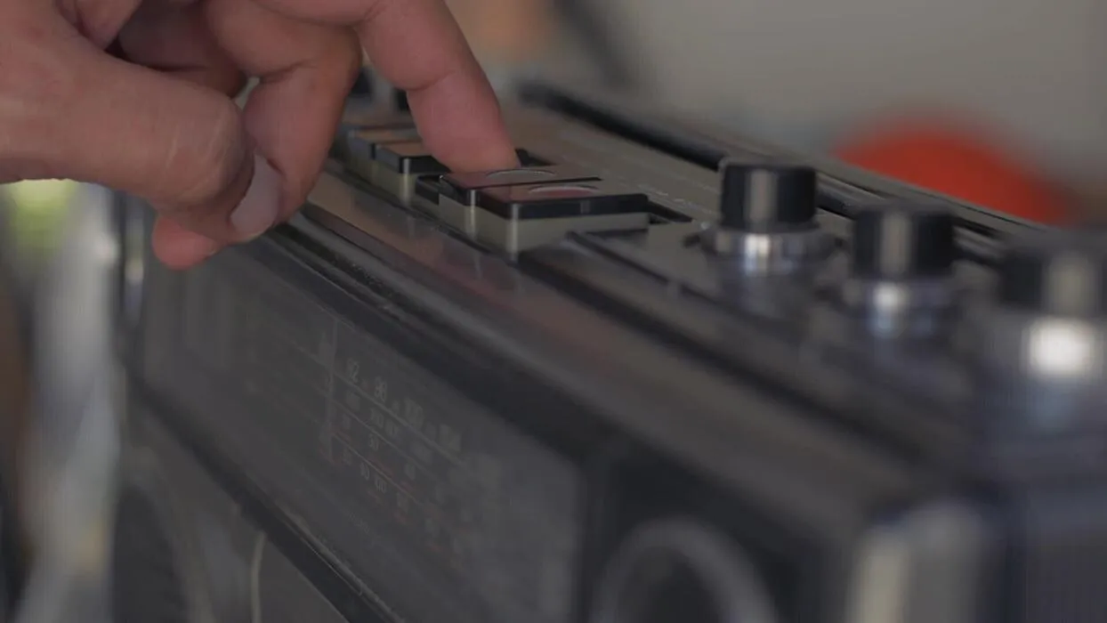 A hand pressing the play key on a 1980s boombox.
